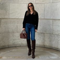 Nikki wears a black sweater, jeans, brown knee-high boots, and a brown bag.