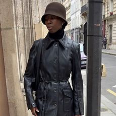 Woman wearing black leather coat with brown hat on the streets of Paris.