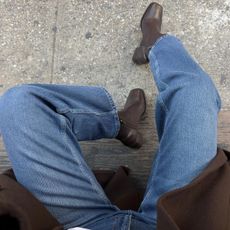 A woman wears brown boots, jeans, and a brown coat.