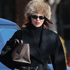 Kendall Jenner spotted in Aspen with Hailey Bieber and Fai Khadra on January 15, 2025 wearing an hourglass blazer by Alaïa with black Commando leggings and knee-high riding boots from Ann Demeulemeester. She accessorized with sunglasses, a brown fur hat, and a brown The Row bag.