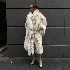 Woman wearing cream faux fur coat and matching ivory leather knee-high boots.